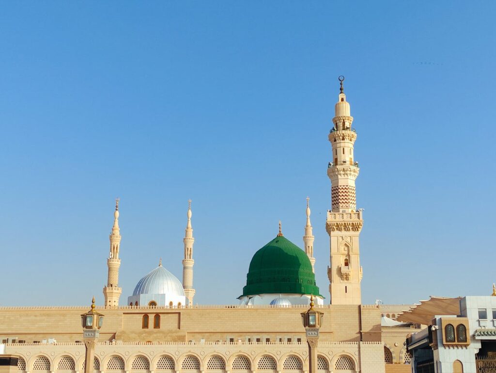 Scenic view of the Prophet's Mosque in Medina, showcasing its iconic minarets and dome under a clear blue sky.